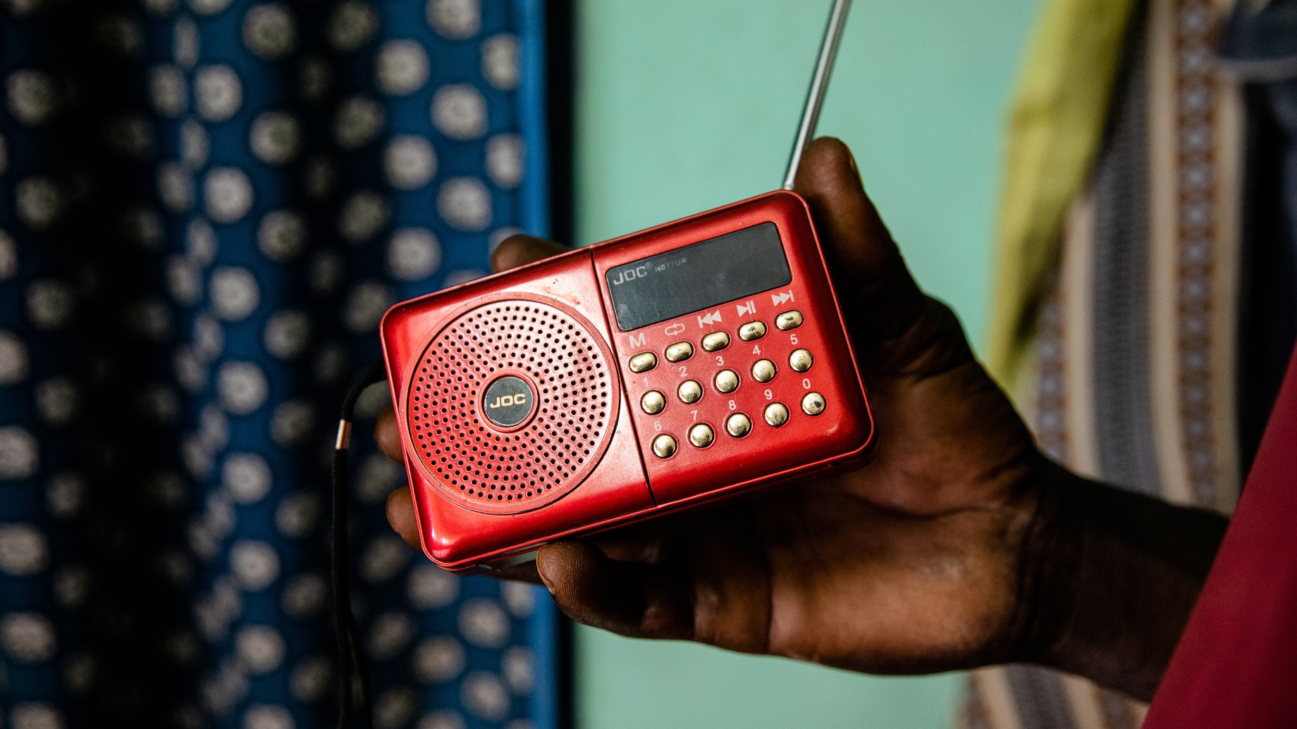 Man's hand holding red radio in front of turquoise wall and polka dot curtain