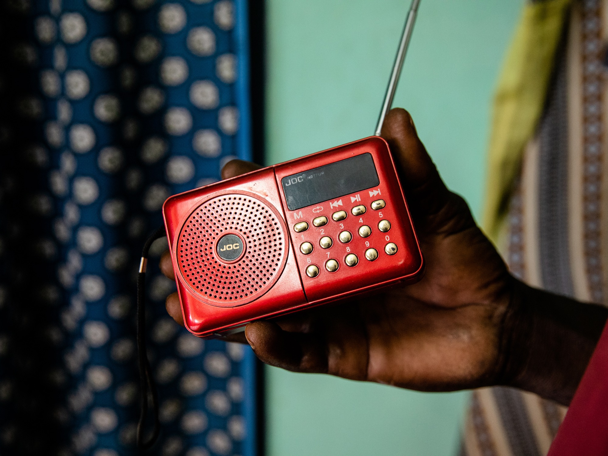 Man's hand holding red radio in front of turquoise wall and polka dot curtain