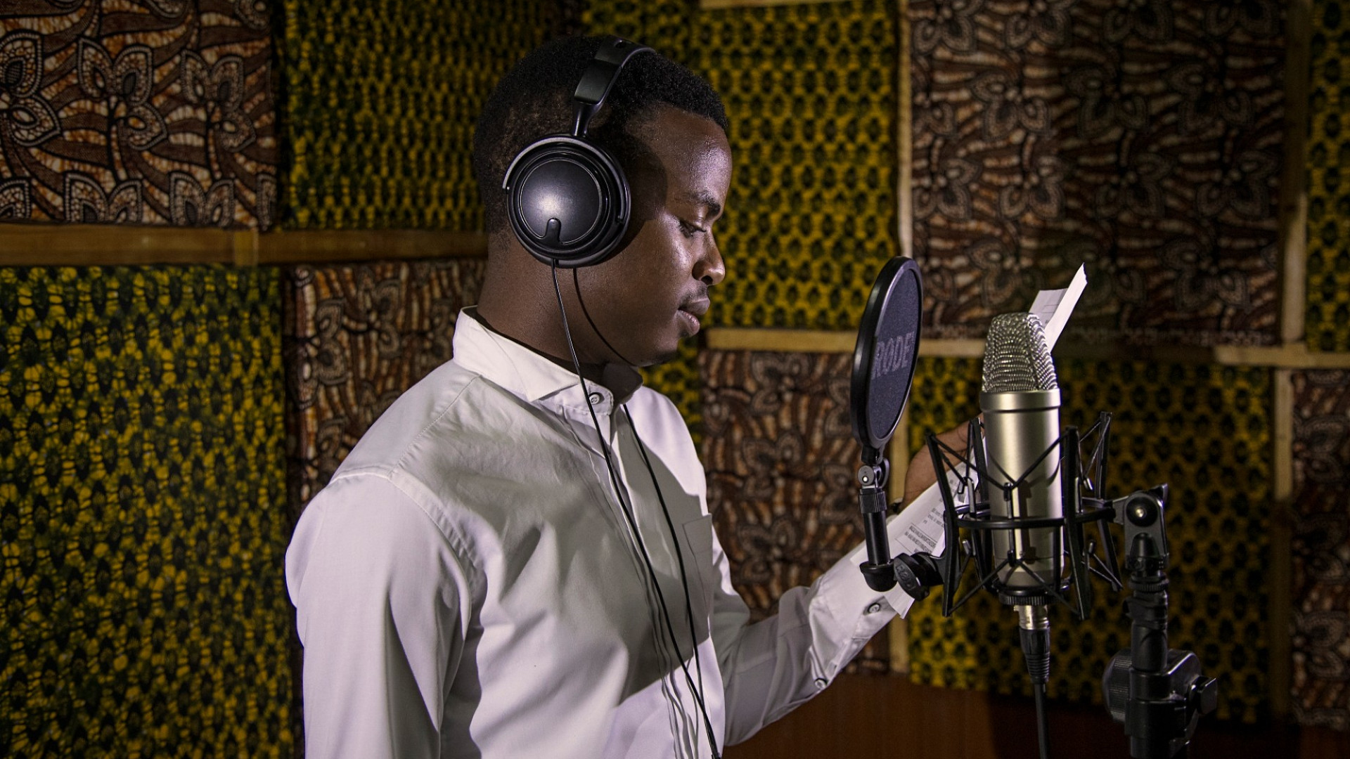 Man wearing headphones reading from script in recording studio